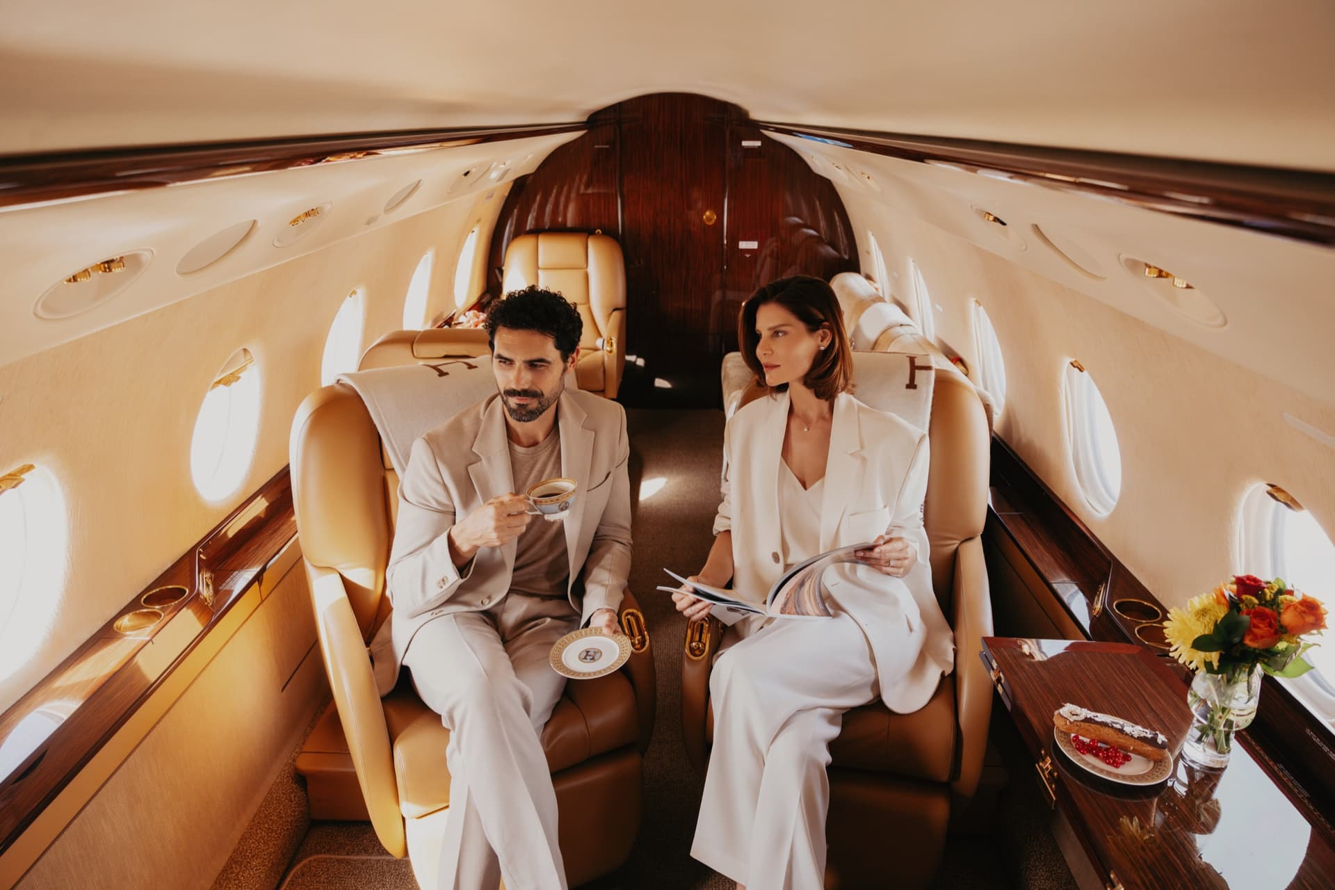 Guests taking coffee in a Gulfstream cabin with cream leather seats and polished wood cabinetry