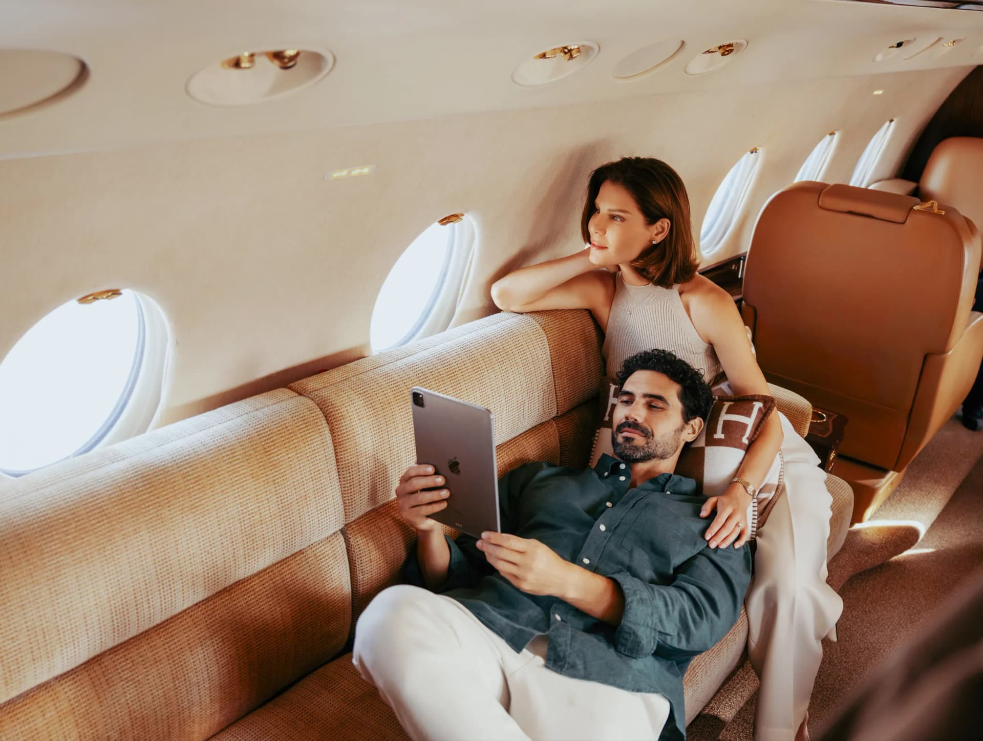 Two guests relaxing on the aft divan of the Gulfstream G200, one reading a tablet