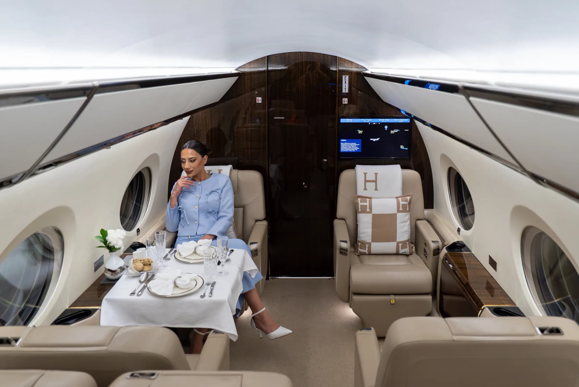 A guest dining at a dressed table in the Gulfstream G450 cabin, beside cream leather seats with Hermès cushions