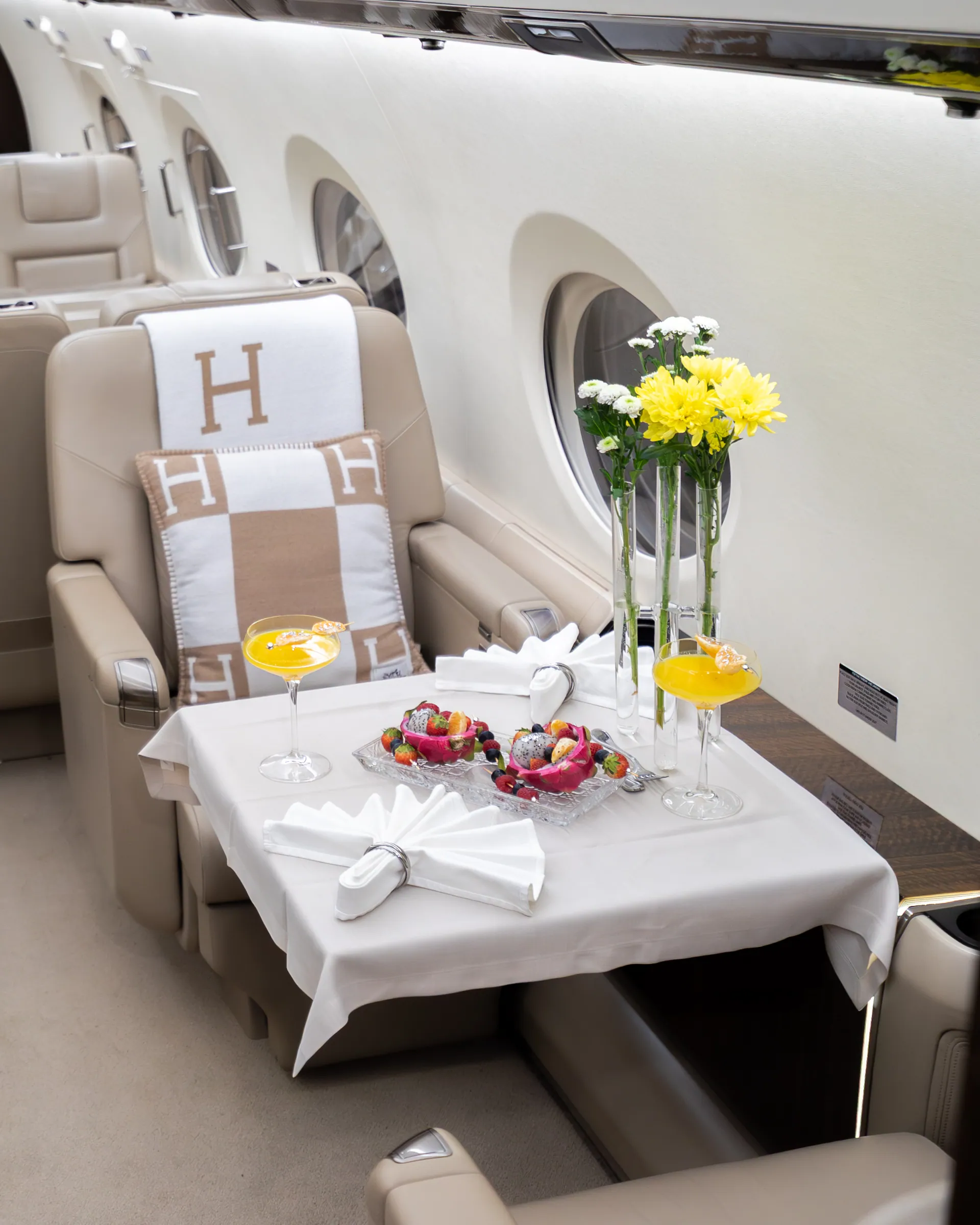 A dressed table with fruit, drinks and yellow flowers beside a Hermès-dressed seat in the Gulfstream G450