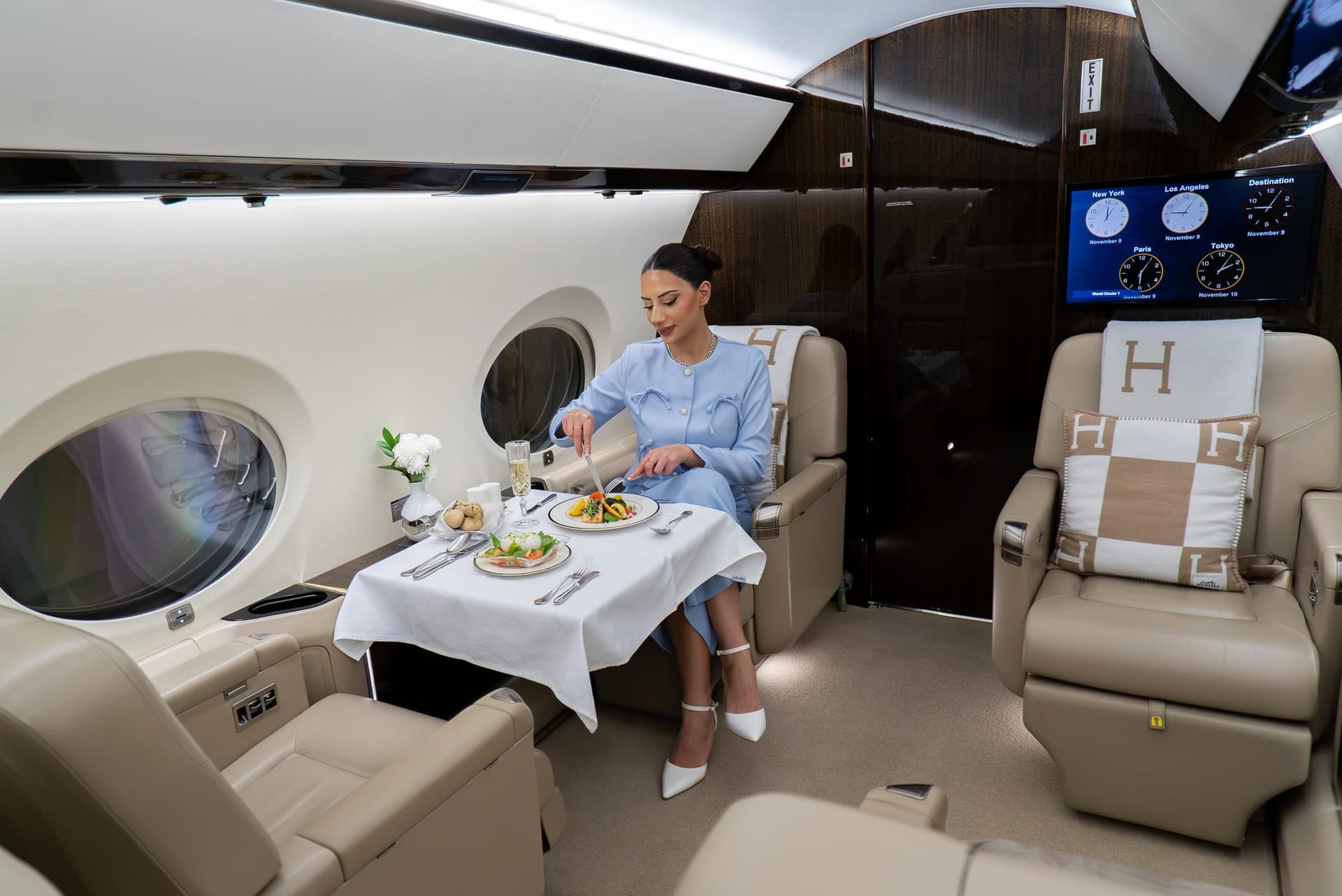 A guest dining at a dressed table in the Gulfstream G450 cabin, with world clocks on the bulkhead